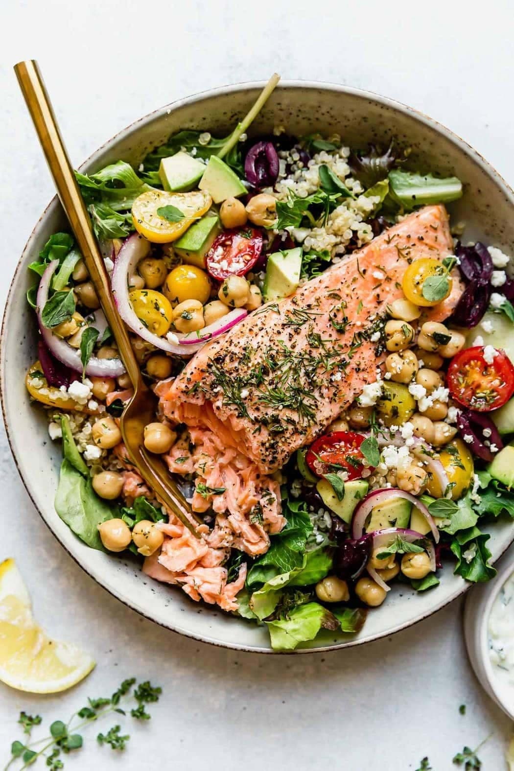 A Mediterranean grain bowl with salmon, cucumber, tomato, and greens, shot from above.
