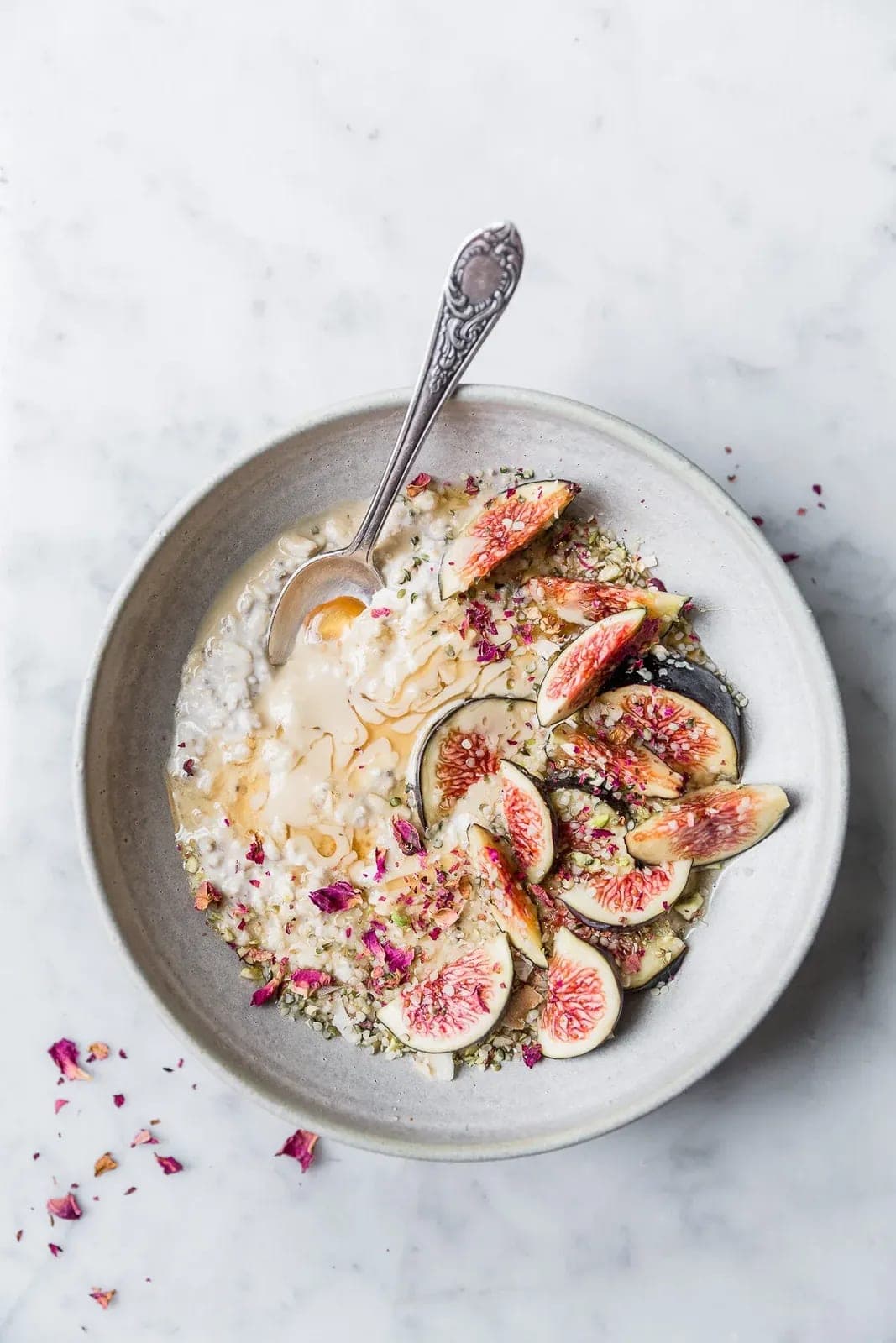 A ceramic bowl of overnight oats drizzled with tahini and honey, topped with sliced fresh figs, pistachios, and hemp seeds.