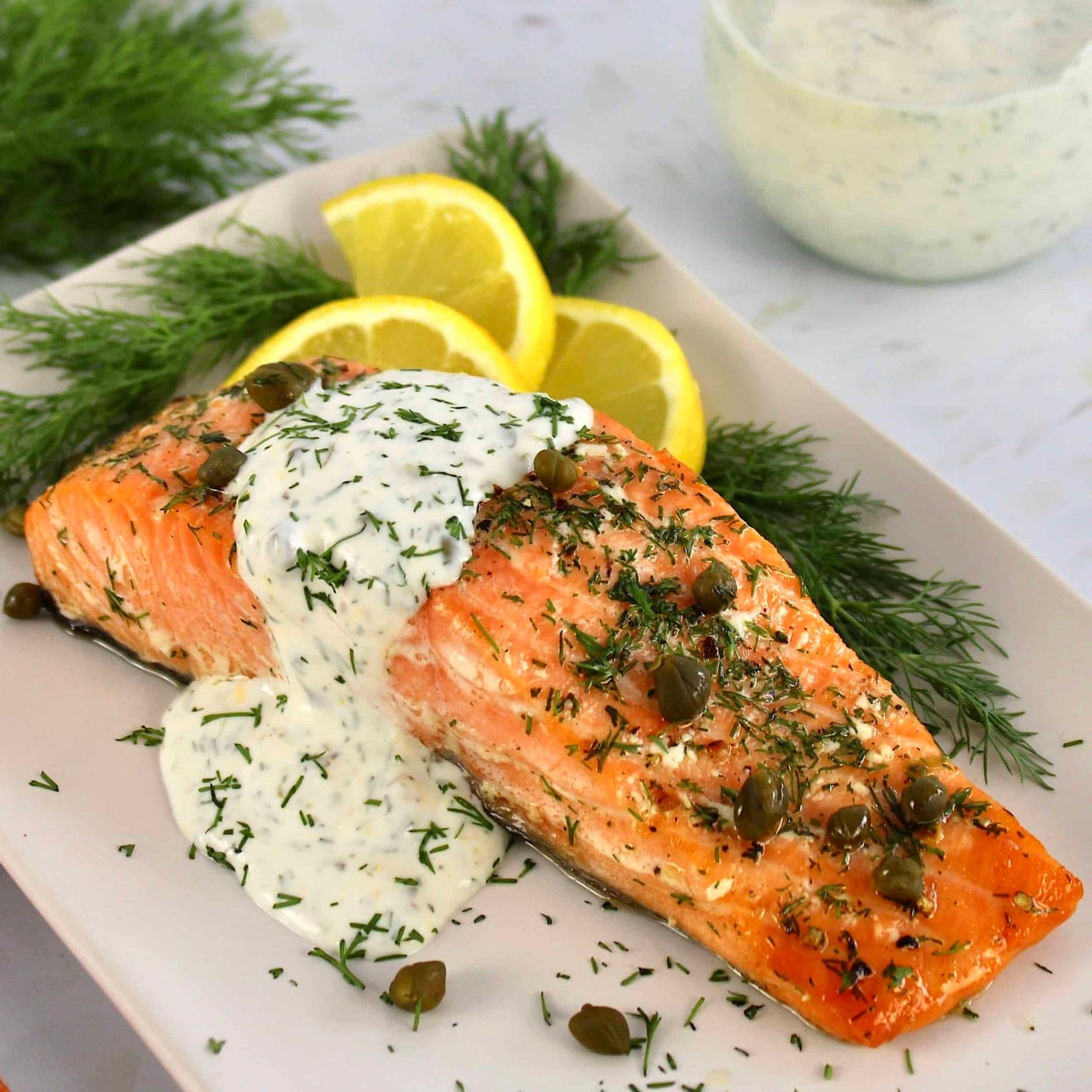 A baked salmon fillet with lemon, capers, and dill under a creamy herb sauce.