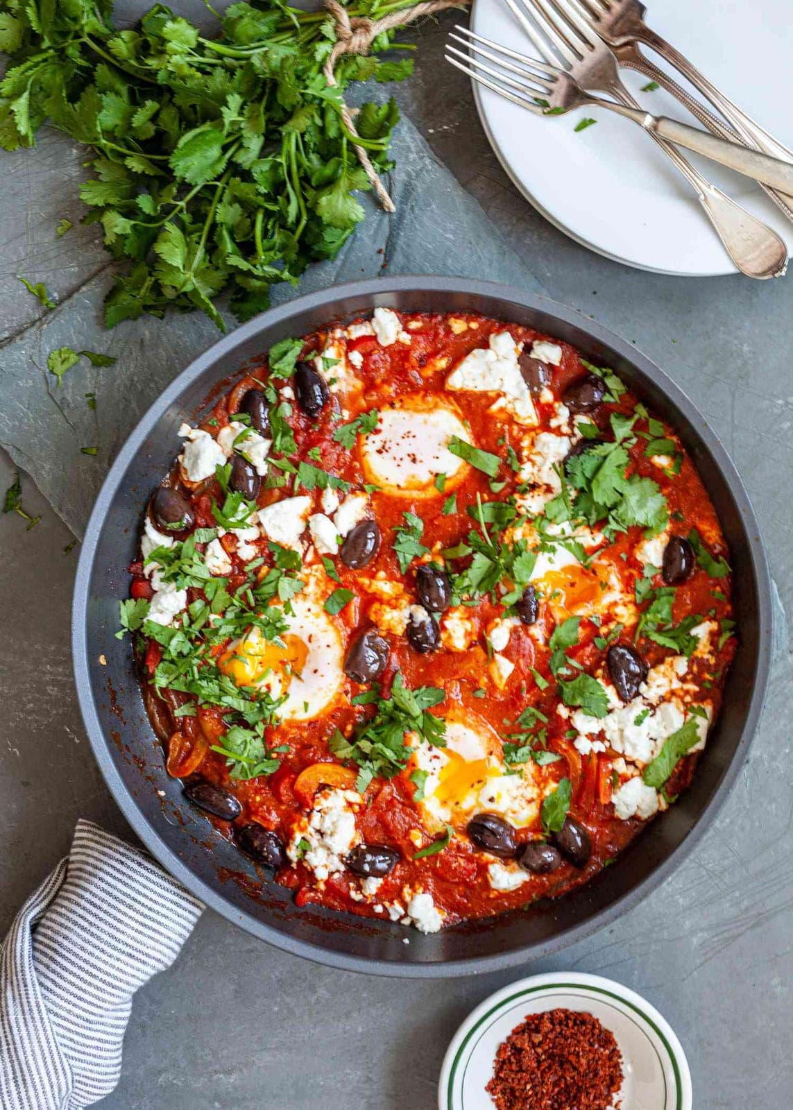 Shakshuka in a cast-iron skillet: eggs poached into spiced tomato sauce, scattered with feta and black olives.